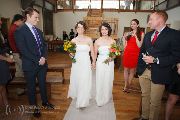 Two Brides Wearing White Wedding Gowns Walk Down the Aisle