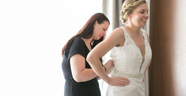 Aisle Less Traveled associate coordinator Kelly zips Kiley into her wedding gown. Photo: Christy Tyler Photography