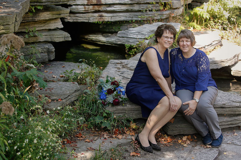 Mary and Pam, both wearing navy, are seated on some wide, flat rocks at Chicago's Lily Pool