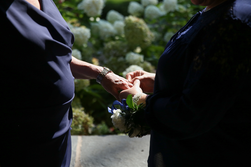 Pam, right, wearing a navy blouse, places a ring on Mary's finger. Mary stands at left and also wears navy.