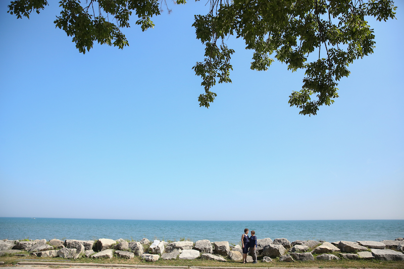 Two women, both wearing navy, stand along the rocky shore of Lake Michigan