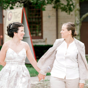 Bride in dress and Bride in suit hold hands