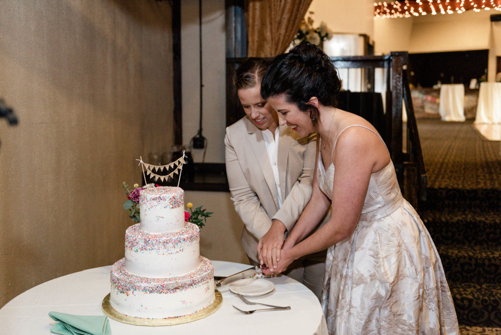 Two brides cut rainbow sprinkle wedding cake