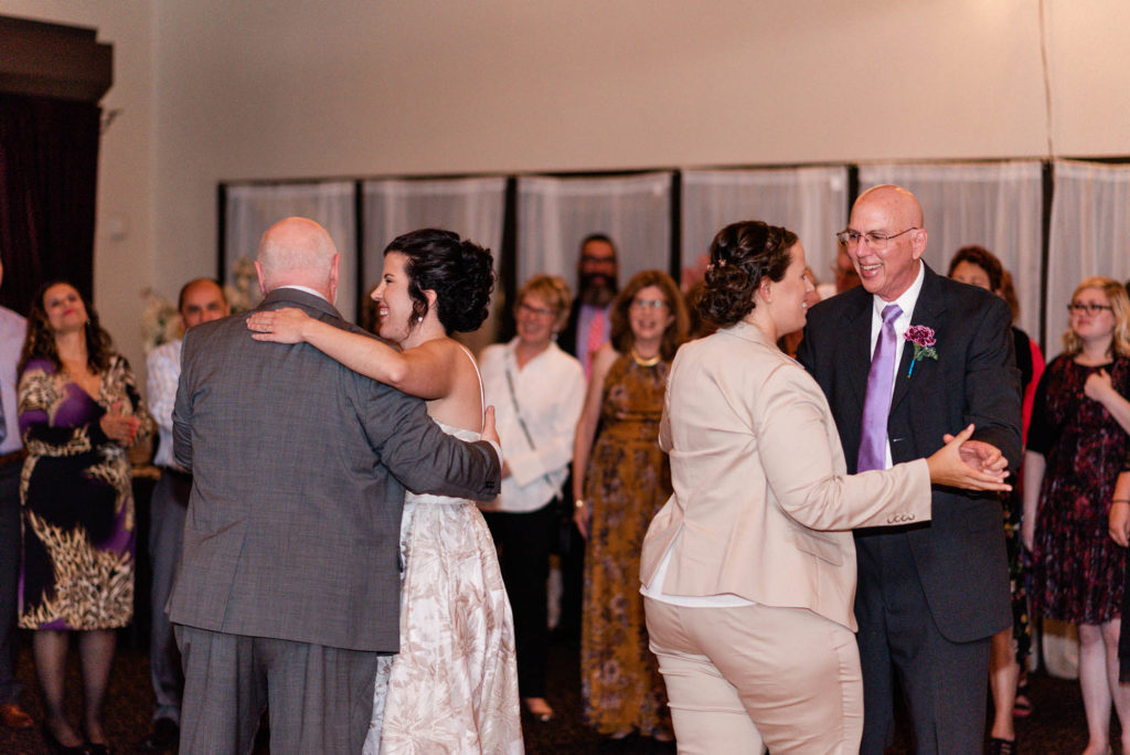 Two brides dance with their dads at wedding reception