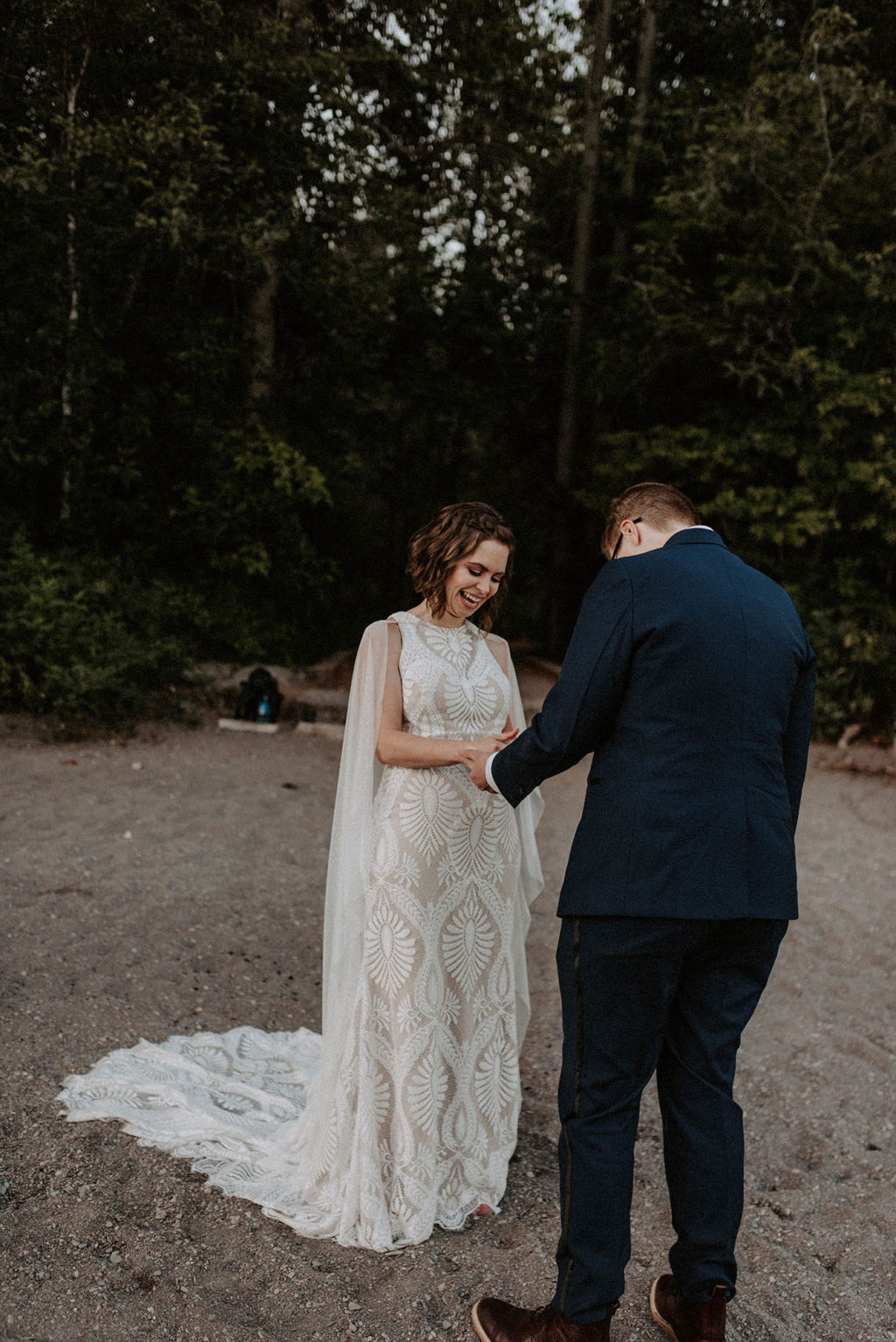 bride reads wedding vows to her wife at beach ceremony in front of forest