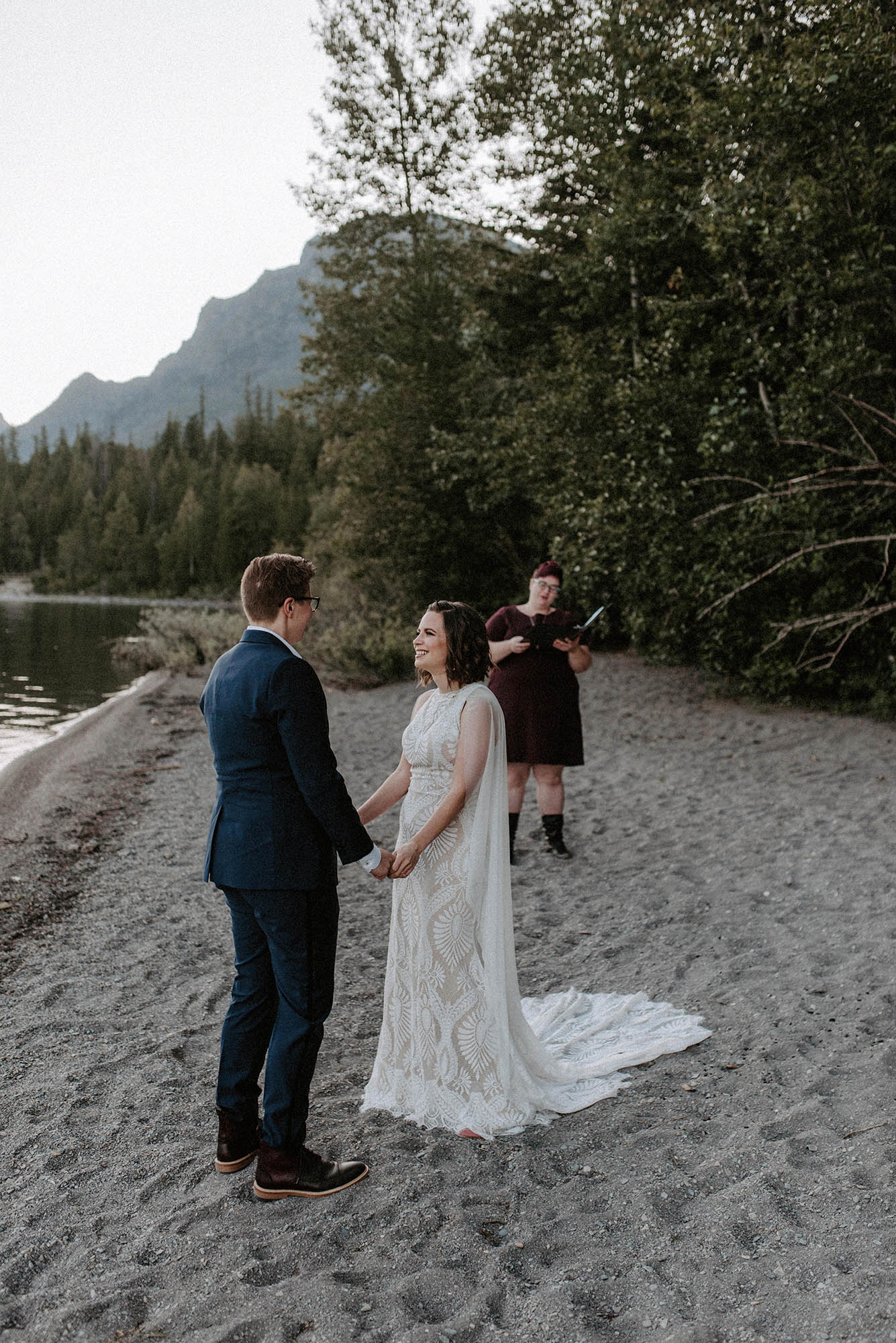 two brides hold hands while officiant performs wedding ceremony on the beach