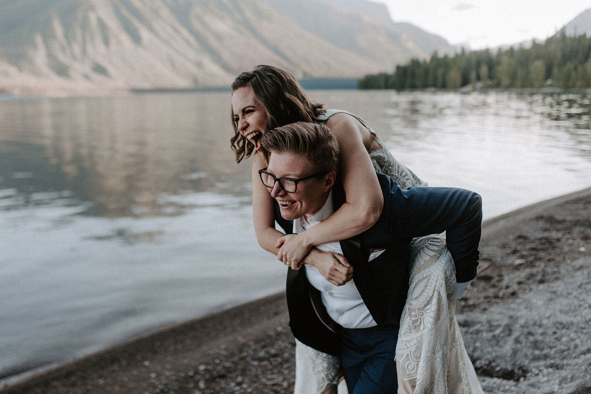 two brides laughing piggyback at Glacier National Park