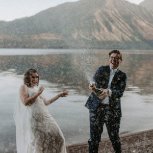 two brides spray champagne over the beach at Lake McDonald