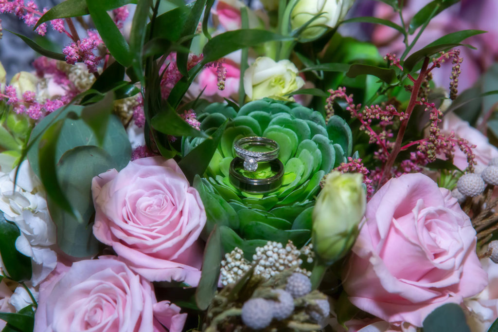 diamond engagement ring and wedding rings on pink and green bridal bouquet