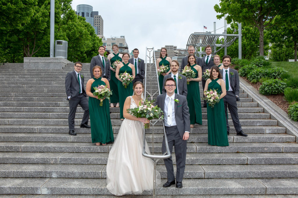 wedding party in green bridesmaid dresses and groomsmen suits with bride and groom on concrete steps in Cincinnati