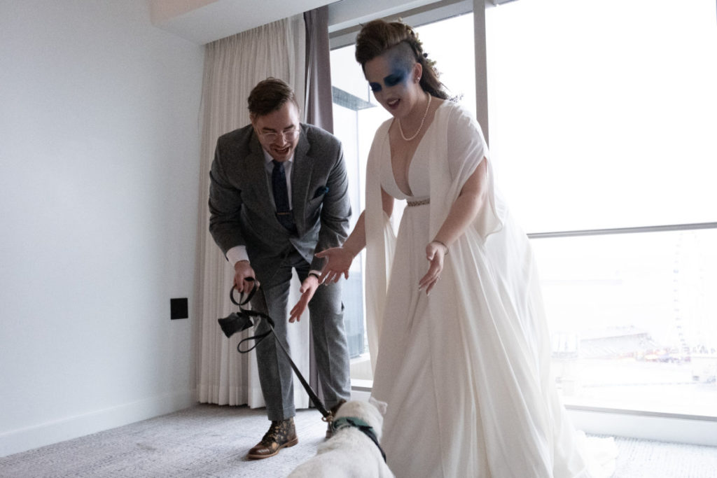 bride in a cape and groom greet their dog at first look