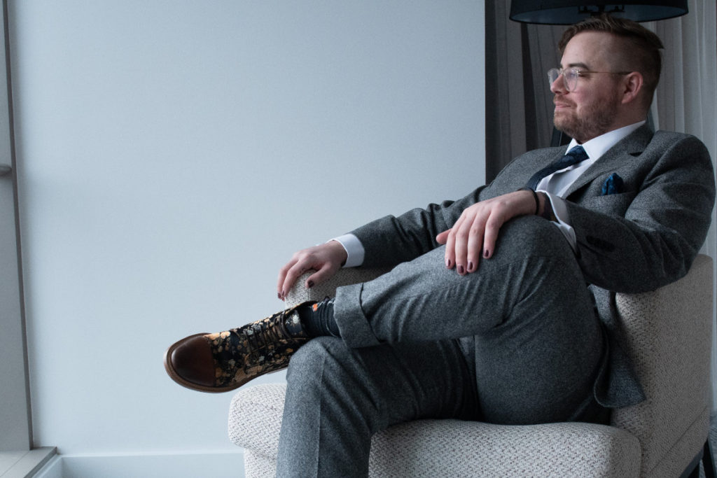 groom with painted fingernails and floral shoes sits in chair