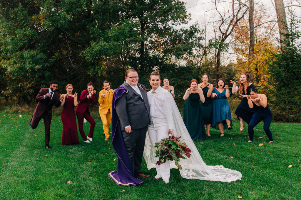 non-binary couple with wedding capes and rainbow wedding party