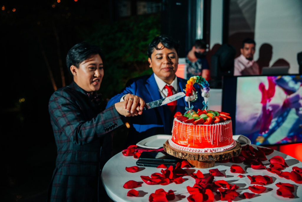 two brides in suits cut rainbow wedding cake