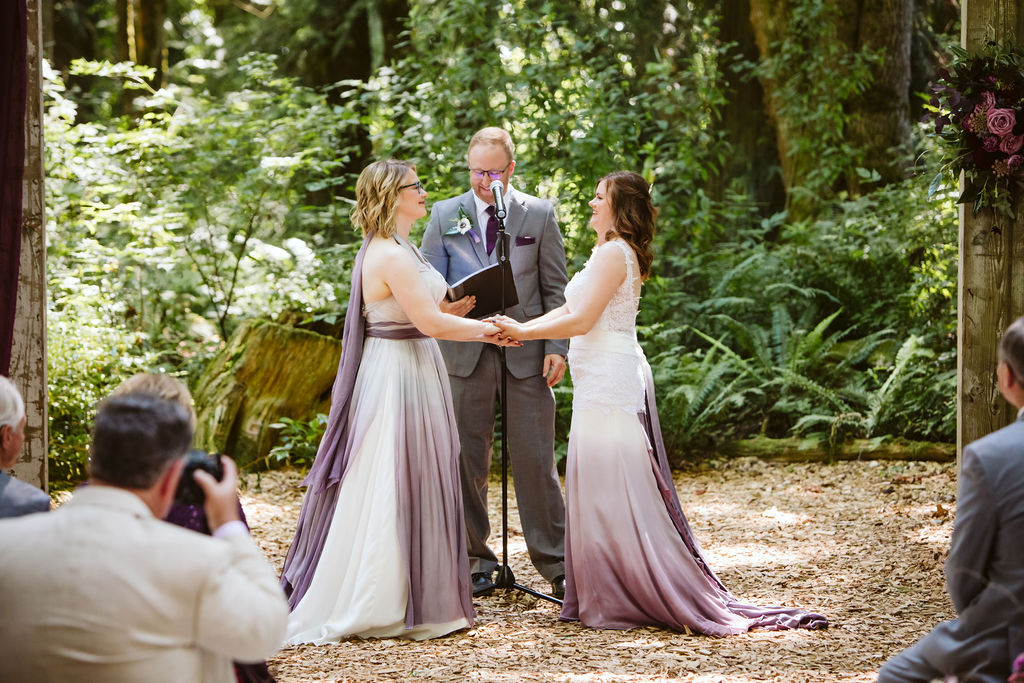 brides in purple ombre dresses hold hands during wedding ceremony
