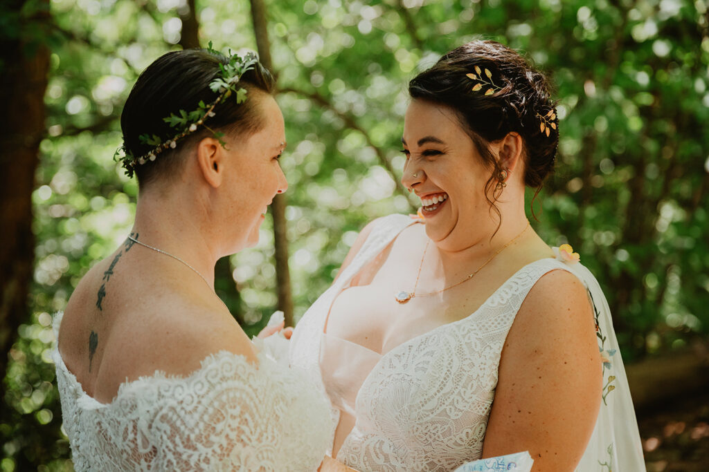 two brides smile at each other in the woods