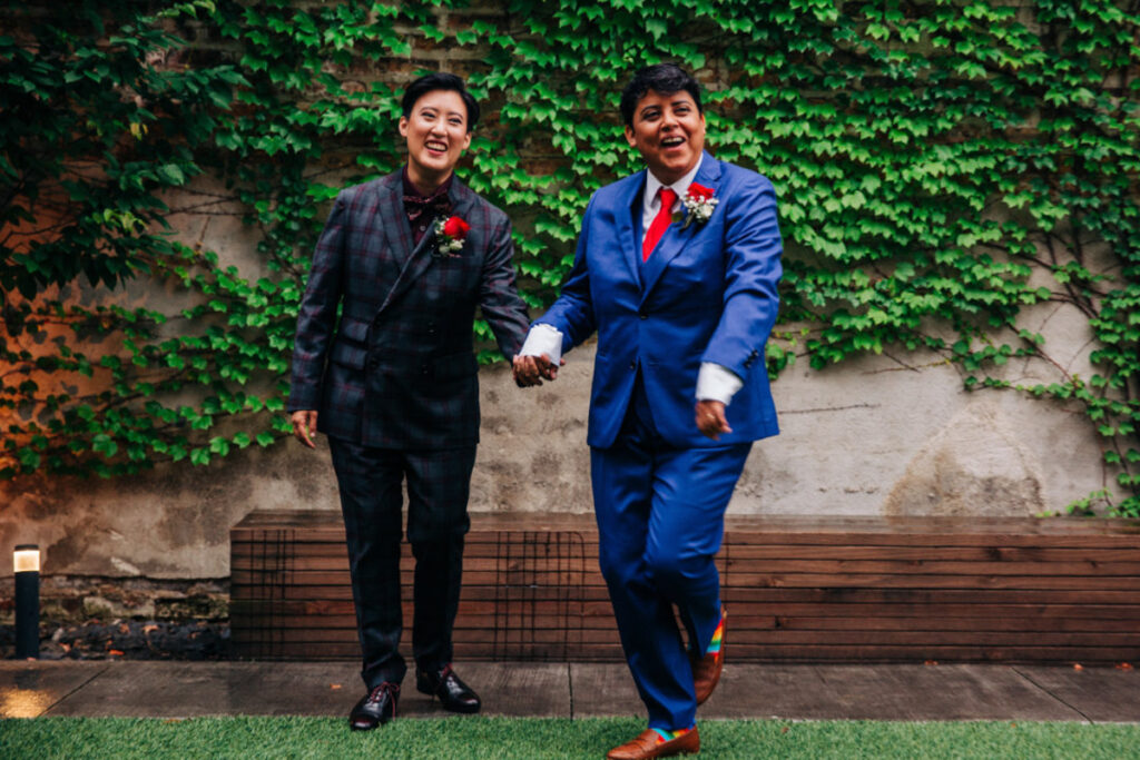 Bride in blue suit and bride in plaid suit with red rose boutonn