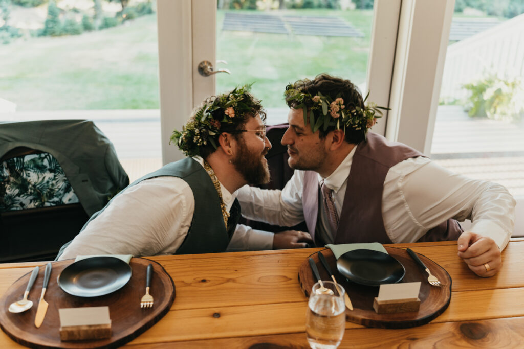 two grooms crouch under a table and kiss at Trinity Tree Farm wedding
