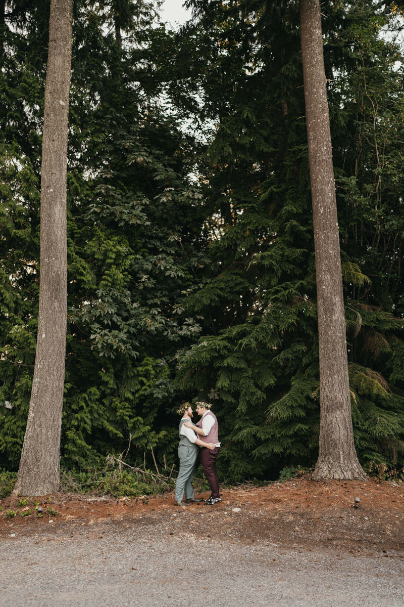 two grooms embrace in front of tall evergreen trees at Trinity Tree Farm wedding