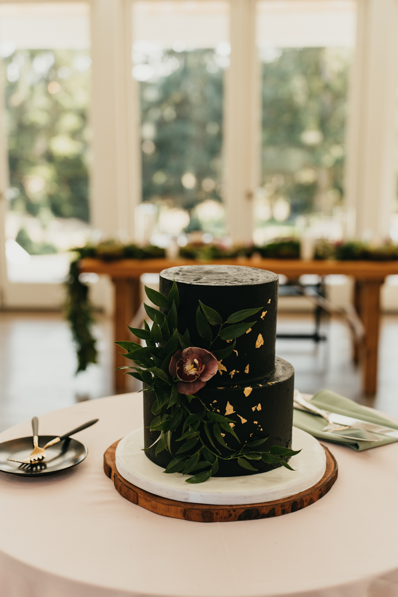 black buttercream wedding cake with edible gold flecks and fresh pink orchid and greenery 