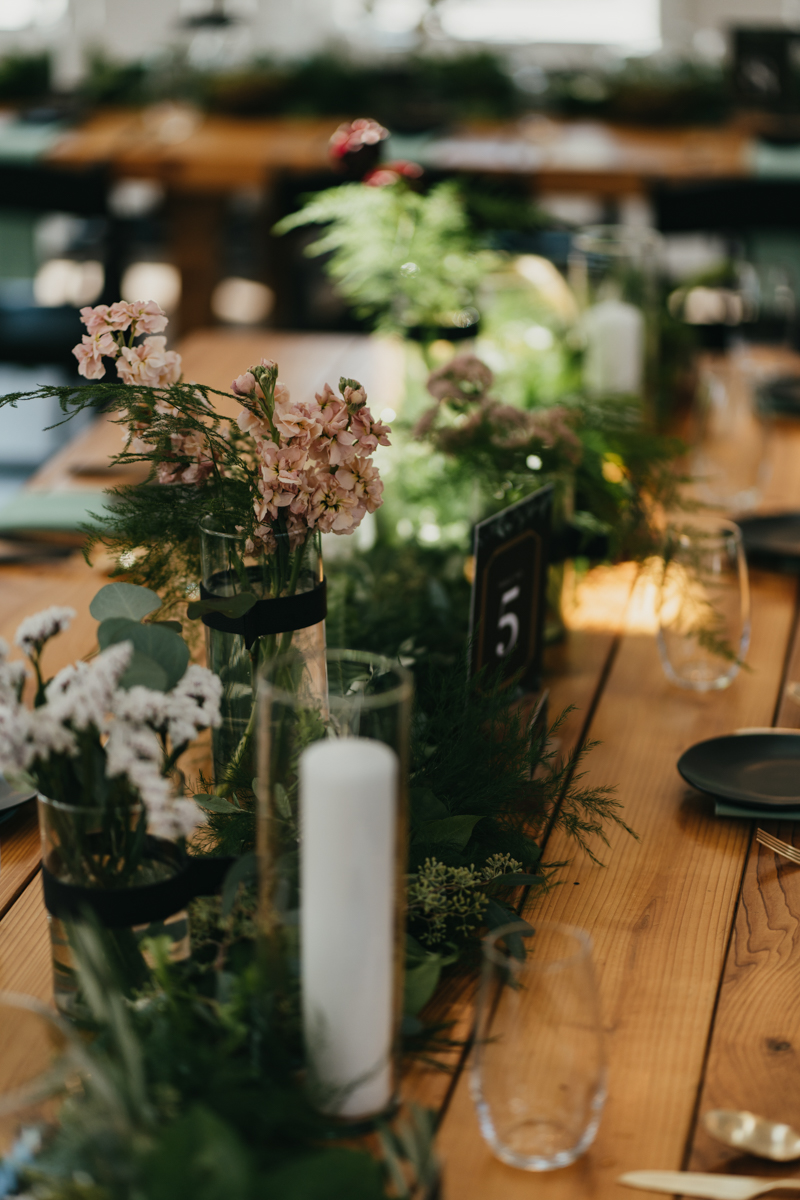 moss and greenery centerpieces and candles on a wood farm table