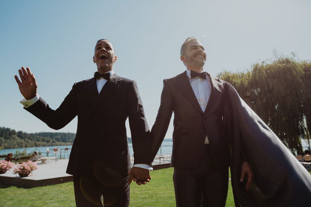 Andy and Victor wearing tuxes and walking and smiling at their wedding