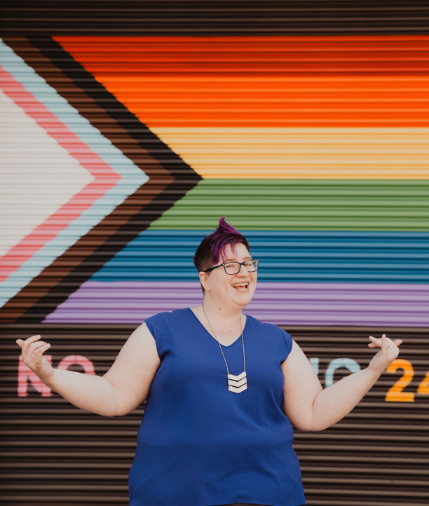 Cindy Savage, LGBTQ+ wedding planner in Seattle and owner of Aisle Less Traveled, standing in front of a pride flag mural
