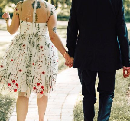couple walking on brick path with bride wearing floral short wedding dress